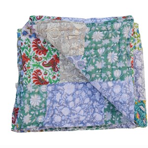 May include: A folded patchwork quilt featuring floral and paisley designs in green, blue, red, and grey. The quilt's different fabric patterns are visible, with visible stitching. The quilt's design gives it a handcrafted appearance.
