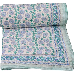 Könnte beinhalten: Eine aufgerollte Steppdecke mit floralem Muster. Die Steppdecke hat einen weißen Hintergrund mit einem sich wiederholenden Muster aus blauen Blumen und grünen Blättern. Der Rand ist hellgrün mit einem blauen Blumendesign. Die Steppdecke ist aus weichem Material.