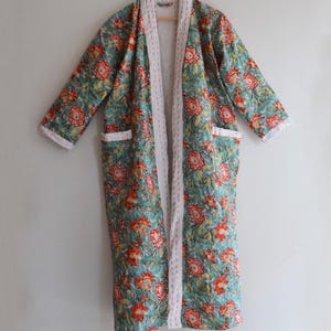 以下が含まれることがあります： ターコイズ、赤、黄色の花柄の長いキルトローブ。ローブは縁とポケットに白いトリムが付いています。ローブは木製のハンガーに掛けられています。