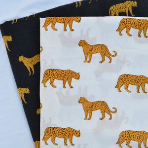 May include: Two fabric pieces are shown, one black and one white. The black fabric has a repeating pattern of yellow leopards. The white fabric also features a repeating pattern of yellow leopards. The leopards are depicted in a standing pose.