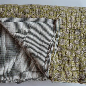 May include: A folded, quilted blanket. The top side has a floral design on a green background, while the reverse features black and white vertical stripes. The blanket is made of soft fabric and is suitable for a bed or sofa.
