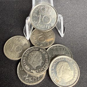 May include: A collection of Dutch coins, including 10 Cent pieces from 1977 and earlier. The coins feature a crown design and the text "10 CENT". Some coins display the profile of a person and the text "KONINGIN DER NEDERLANDEN".