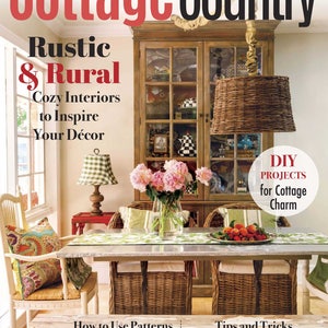 Puede incluir: Una portada de revista para Cottage Country que presenta un comedor r&uacute;stico con una mesa de madera, sillas de mimbre y un gran armario de madera. El texto de la portada de la revista dice "Rustic & Rural Cozy Interiors to Inspire Your D&eacute;cor".