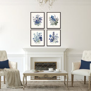 May include: Four framed botanical art prints featuring blue and purple floral arrangements. The prints are displayed above a white fireplace, with two cream-colored armchairs and a coffee table in front. The room is decorated in a classic style.