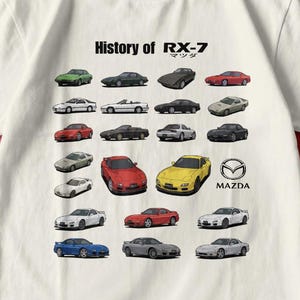 Puede incluir: Camiseta blanca con un gráfico de varios modelos de coches Mazda RX-7. La camiseta tiene el texto "History of RX-7" encima de las ilustraciones de los coches y el logotipo de Mazda. Los coches son de varios colores, incluyendo rojo, amarillo y azul.
