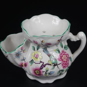 May include: White ceramic shaving scuttle with a floral and bird design. The scuttle features a handle, a soap dish, and a bowl with a scalloped rim. The floral pattern includes pink, yellow, and blue flowers with a bird.