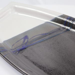 Peut inclure: Plat à servir rectangulaire en céramique avec un design bicolore. La moitié supérieure est blanche, passant à une base grise texturée avec des accents bleus. Le plat a un bord légèrement surélevé.