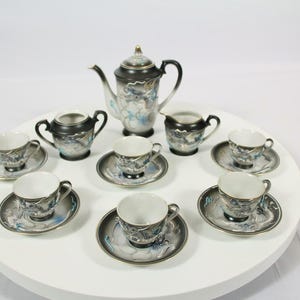 May include: A tea set comprising a teapot, a sugar bowl, a creamer, and six cups with matching saucers. Each piece is crafted from black and white ceramic with a detailed blue and grey dragon motif and gold trim accents on the rims and handles.