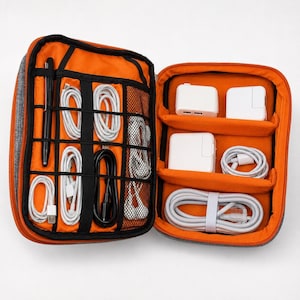 May include: Open, gray and orange travel organizer with multiple compartments. The left side holds a black pen, white and black cables, and mesh pockets. The right side contains white power adapters and more cables.