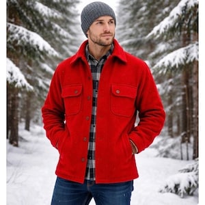 May include: A bright red wool jacket with two chest pockets and button closures. The jacket is worn over a plaid shirt and blue jeans. A gray beanie is worn on the head. The background is a snowy forest.
