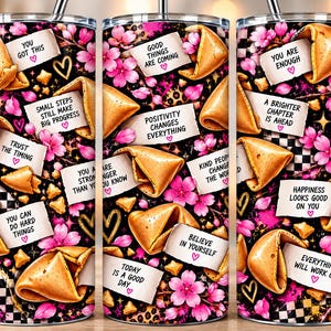 Könnte beinhalten: Ein zylindrischer Edelstahlbecher mit Strohhalm, verziert mit einem schwarz-weißen Schachbrettmuster, rosa Kirschblüten und goldenen Herzumrissen. Das Design zeigt mehrere Glückskekse mit weißen Zetteln, die motivierende Texte enthalten.