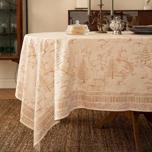 May include: A round tablecloth featuring a cream-coloured base with a repeating brown print of deer, pine trees, and forest landscapes. The fabric has a decorative border with vertical stripes and intricate scrollwork patterns along the edge.