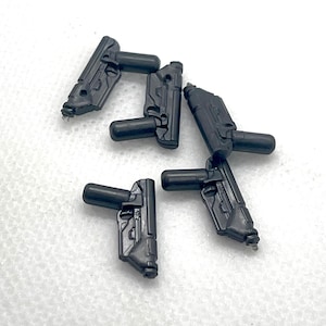 May include: Five small, black toy guns are scattered on a white surface. Each gun has a rectangular body with a handle and a small barrel. The guns appear to be made of plastic.