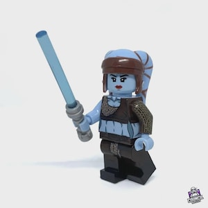 Op de afbeelding: Een Lego-figuur met blauwe huid, bruine kleding en een hoofdband, die een lichtblauw lichtzwaard vasthoudt. De figuur heeft blauw haar en staat tegen een witte achtergrond. De figuur is een Star Wars-personage.