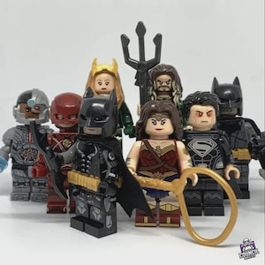 Puede incluir: Colección de minifiguras Lego de superhéroes, incluyendo Batman, Wonder Woman y Superman. Las figuras están en varias poses, con trajes y accesorios detallados. El fondo es blanco liso.
