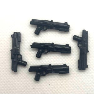 May include: Five black toy blasters are arranged on a white surface. The blasters have a detailed design with a handle, trigger, and barrel. The toys are made of plastic and are likely for play or display.