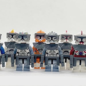 May include: A group of Lego clone trooper minifigures, each with detailed armour and helmets. The figures display a range of colours, including blue, orange, and red accents, and are set against a white backdrop.