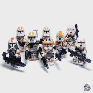 Puede incluir: Un grupo de ocho minifiguras de Lego, cada una representando a un soldado clon con armadura blanca, naranja y gris. Las minifiguras sostienen blasters negros y otros accesorios. El logotipo de Council Bricks está en la esquina inferior derecha.