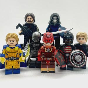 May include: A collection of seven Lego minifigures, each representing a superhero or character. The figures are in various colors, including red, blue, yellow, black, and gray. Some figures hold weapons or shields, and all have detailed costumes and expressions.