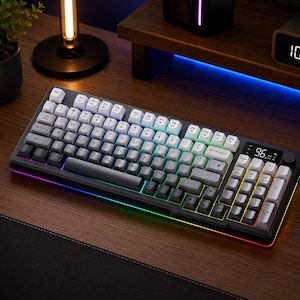 Könnte beinhalten: Eine schwarze und graue mechanische Tastatur mit weißen und grauen Tastenkappen. Die Tastatur hat einen Regenbogen-LED-Lichtstreifen an den Rändern und ein digitales Display mit der Anzeige "96.". Die Tasten sind mit einem Regenbogen-Farbverlauf hinterleuchtet.