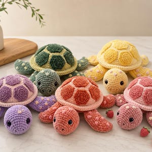 May include: Five crocheted turtle plushies in purple, dark green, yellow, orange, and pink. Each turtle features a textured shell with a hexagonal pattern, a rounded head with black eyes, and flippers decorated with small, lighter-colored spots.