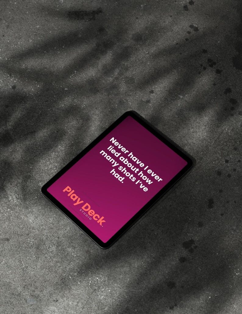 以下が含まれることがあります： 「Play Deck Studio」のゲームカード。マゼンタ色の背景に「Never have I ever lied about how many shots I've had.」のテキスト。カードは黒い縁取りで、灰色の表面に置かれています。