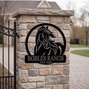 Op de afbeelding: Een rond bord van zwart metaal met een uitgesneden silhouet van een paardenkop en manen. Onder de cirkelvormige rand bevindt zich een rechthoekige plaat met de tekst ROBLES RANCH in hoofdletters, met daaronder gecentreerd EST 2020.