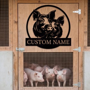 May include: A black metal sign featuring two pig faces within a circle, with the text "CUSTOM NAME" below. The sign is mounted on a wooden door, with several pink piglets visible behind a wire mesh.