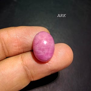 Può includere: Una gemma rosa lucida di forma ovale. La pietra ha una superficie liscia e un aspetto leggermente traslucido. Il testo "ARK" è visibile nell'angolo in alto a destra. La gemma è tenuta tra due dita.
