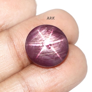 Könnte beinhalten: Ein runder, polierter Sternrubin-Edelstein. Der Edelstein hat eine tiefrote bis violette Farbe mit einem sechsstrahligen Sternmuster auf der Oberfläche. Das Wort "ARK" ist im Hintergrund sichtbar.