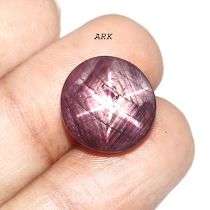 Könnte beinhalten: Ein runder, polierter, purpurroter Edelstein mit einem sechsstrahligen Sternmuster. Der Edelstein wird in einer Hand gehalten, und der Text "ARK" ist in der oberen linken Ecke sichtbar. Das Sternmuster ist weiß und deutlich sichtbar.