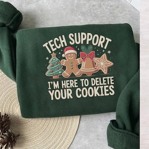 May include: A dark green sweatshirt with the text "TECH SUPPORT" above a graphic of a Christmas tree, gingerbread man, bell, and star cookie. The text "I'M HERE TO DELETE YOUR COOKIES" is below the graphic.