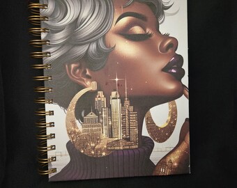 Könnte beinhalten: Spiralgebundenes Notizbuch mit einer Illustration einer Frau mit silbernem Haar und goldenen Creolen. Die Ohrringe und der Raum in ihnen zeigen eine Stadtlandschaft. Die Frau trägt einen lila Rollkragenpullover.