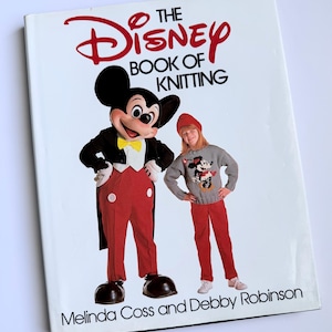 May include: A book cover for "The Disney Book of Knitting" featuring Mickey Mouse in a tuxedo and a child in a Mickey Mouse sweater and red pants. The book's title is in red script, with the authors' names at the bottom.