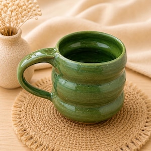 May include: A glossy, forest green ceramic mug with a distinct three-tiered, rounded, stacked shape and a curved handle. The mug features a smooth, reflective glaze finish and a wide, open circular rim, showcasing a handmade, artisanal aesthetic.