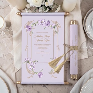 Könnte beinhalten: Eine hellviolette Hochzeitseinladung als Schriftrolle mit Goldfolienakzenten und violetten Aquarellblumen. Der Text lautet Shuhua Zhang und Ziming Yan. Die Rolle ist mit einer goldenen Kordel und zwei goldenen Quasten sowie Endkappen versehen.