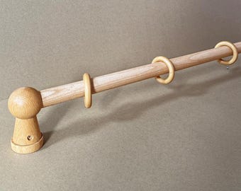 May include: A wooden curtain rod with a light brown finish. The rod features a decorative finial on one end and several wooden rings for hanging curtains. The rod is made of solid wood and has a simple, classic design.
