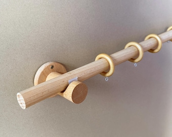 May include: A wooden curtain rod with light-colored wood construction. The rod is mounted on a wall and features several wooden rings. The rod is approximately 1.5 inches in diameter.