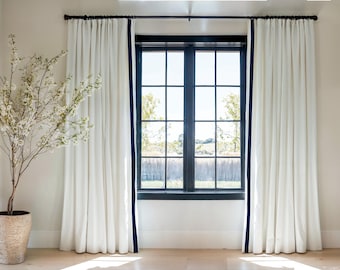 Cortinas de lino y algodón en color blanco crema con ribete azul marino y plisadas.