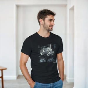 Puede incluir: Camiseta negra con una ilustración estilo plano de un tractor de vapor vintage. El diseño, en azul y blanco, resalta los detalles mecánicos. La camiseta la lleva una persona.