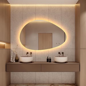 May include: A modern bathroom design featuring a large, oval-shaped mirror with a warm, glowing light. Two white, bowl-shaped sinks sit atop a brown floating vanity. The walls are a neutral beige with vertical textured panels, and the floor has a marble pattern.
