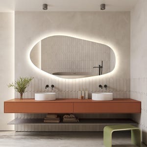 May include: Modern bathroom design featuring a large, illuminated oval mirror. The space includes a burnt orange vanity with two white sinks, a lower shelf, and a green stool. The walls are a neutral color with vertical tile accents, creating a minimalist aesthetic.