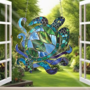 May include: Stained glass sea turtle suncatcher with a mosaic design. The turtle features shades of blue and green, with a decorative chain for hanging. The suncatcher is displayed in front of an open window with a green background.
