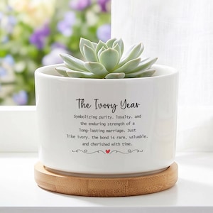 May include: A white ceramic planter with the text "The Ivory Year" and a succulent plant. The planter sits on a round, light brown bamboo coaster. The text describes the enduring strength of a long-lasting marriage.