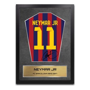 Puede incluir: Obra de arte enmarcada con un diseño de camiseta con el nombre "NEYMAR JR" y el número "11" en amarillo. La camiseta tiene rayas rojas y azules. Una placa dorada en la parte inferior dice "NEYMAR JR FC BARCELONA 2013-2017".