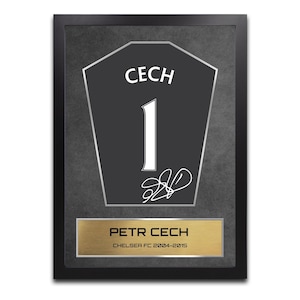 Peut inclure: Œuvre d'art encadrée représentant un maillot noir avec le nom "CECH" et le numéro "1" en blanc. Comprend une plaque dorée avec "PETR CECH" et "CHELSEA FC 2004-2015". L'œuvre est placée sur un fond gris texturé.