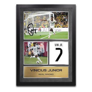 以下が含まれることがあります： サッカー選手ヴィニシウス・ジュニオールの画像が収められた額入りコラージュ。サイン入り写真、アクションショット、名前と背番号7が入ったジャージグラフィックが含まれています。下のプレートには「ヴィニシウス・ジュニオール、レアル・マドリード」と書かれています。