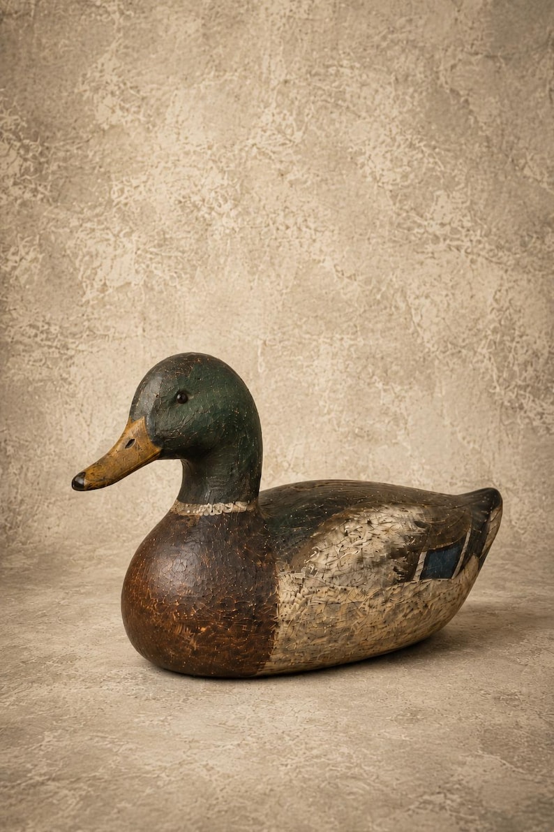 Pode incluir: Um chamariz de pato-real esculpido em madeira com cabe&ccedil;a verde-escura, bico amarelo-acastanhado, peito castanho e corpo com detalhes de plumagem cinzenta e branca texturizada, incluindo uma pequena mancha azul na asa, visto de perfil.