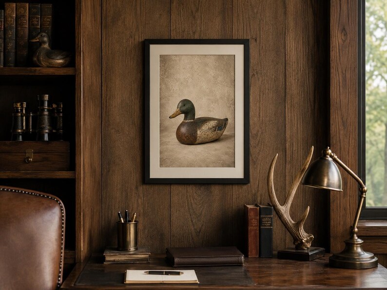 Pode incluir: Uma impress&atilde;o de arte emoldurada apresentando um chamariz de pato-real com cabe&ccedil;a verde, peito castanho e corpo cinzento. A obra de arte &eacute; exibida numa moldura preta simples contra uma parede de pain&eacute;is de madeira escura num escrit&oacute;rio.