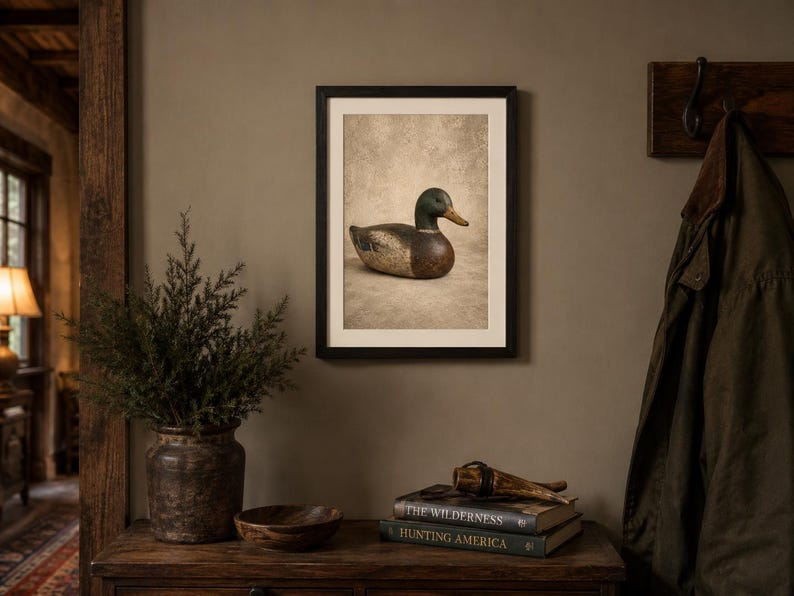 Pode incluir: Uma impress&atilde;o art&iacute;stica emoldurada apresentando um chamariz de pato-real com cabe&ccedil;a verde, peito castanho e corpo cinzento, sobre um fundo texturizado neutro. A obra est&aacute; inserida numa moldura preta simples com uma margem branca.